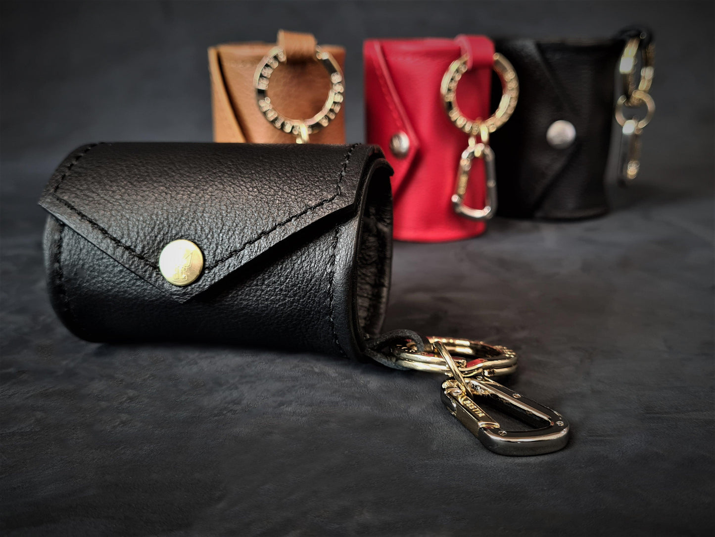 Black leather keychain case dog poop bag holder with gold accents on a dark background